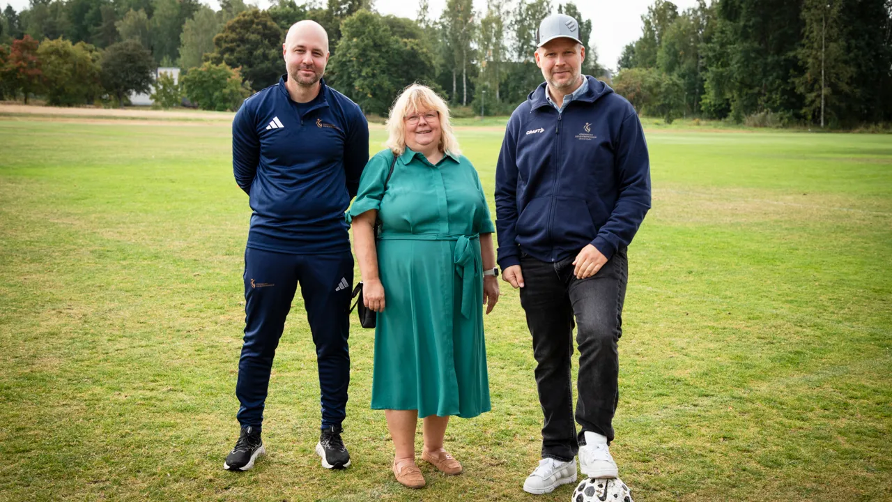 En grupp på tre personer som står bredvid varandra på en fotbollsplan.