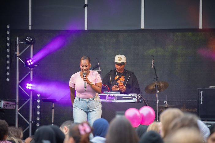En kvinna på scenen som sjunger inför publik. I bakgrunden står hennes DJ.