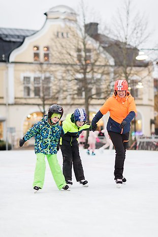 En förälder skrattar tillsammans med sina barn på isen. De har orange och gröna kläder på sig. Foto: Hanna Maxstad