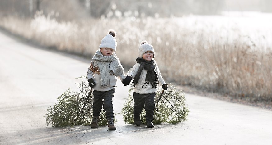Två barn bär varsin gran. Frost i gräset runtomkring.