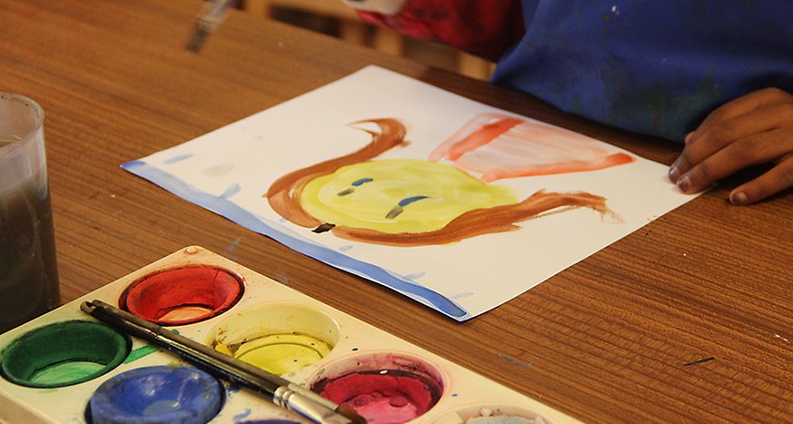 En teckning på ett ansikte ett barns händer och lite vattenfärger